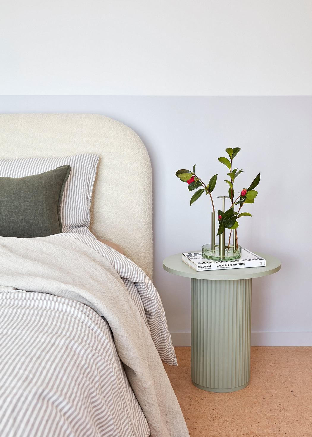 Minimalist bedroom with striped bedding, green cushion, and plant decor on side table.