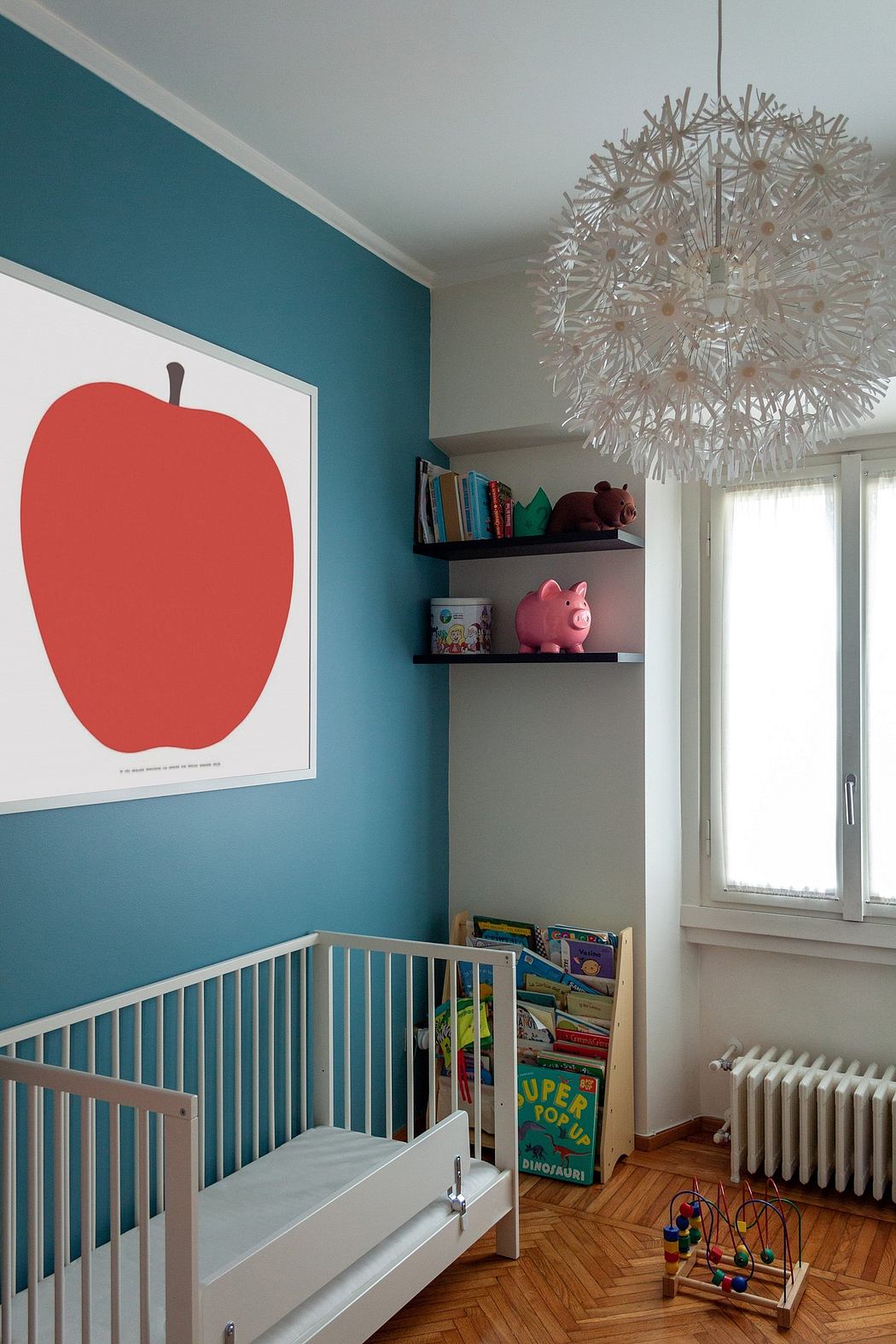 A bright, modern nursery with colorful wall art, a crib, and a playful chandelier.