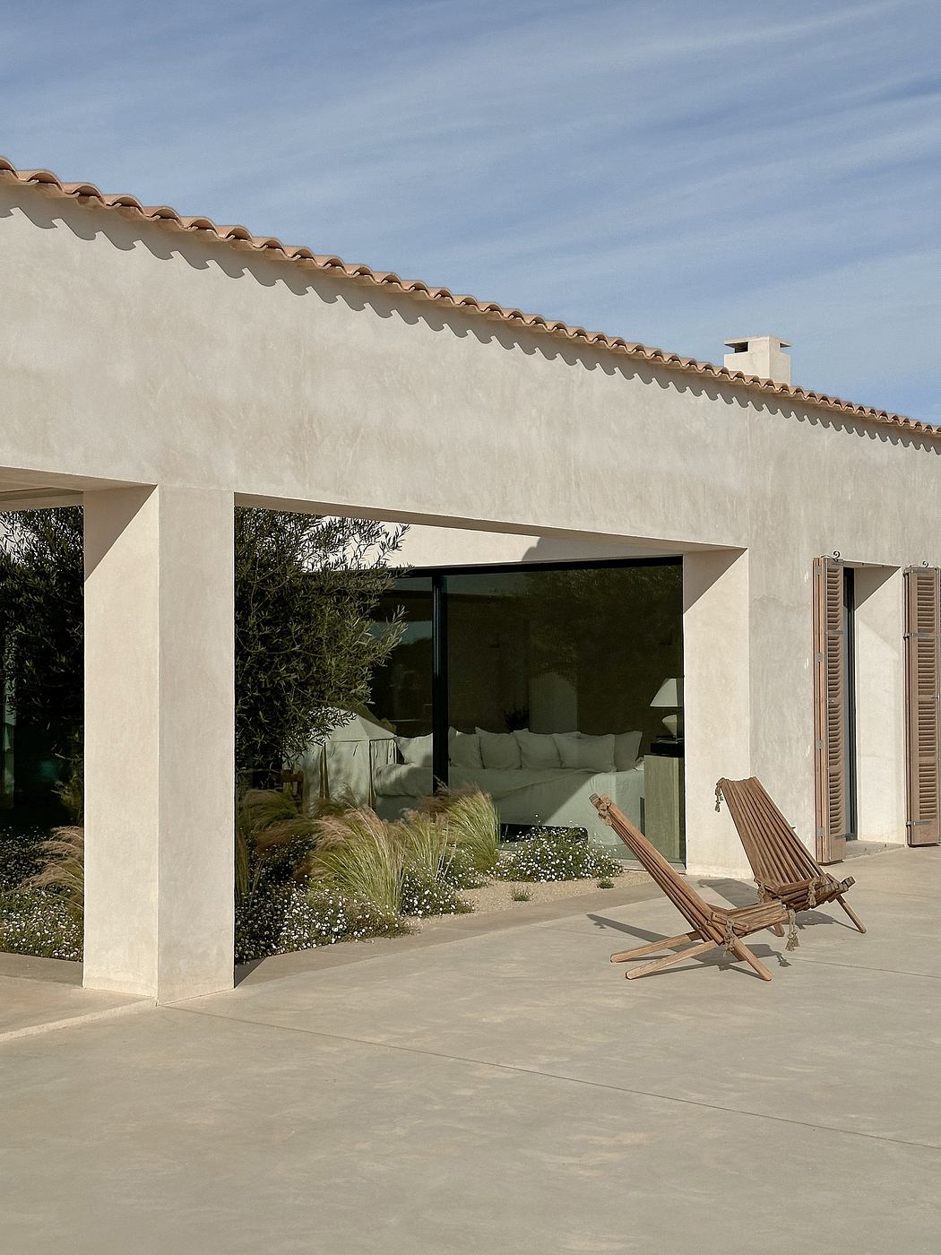 Exterior of a modern Mediterranean-style home with tiled roof, recessed doors, and outdoor seating.