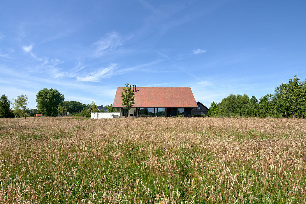 A modern farmhouse with a red-tiled roof, surrounded by a grassy field and trees.