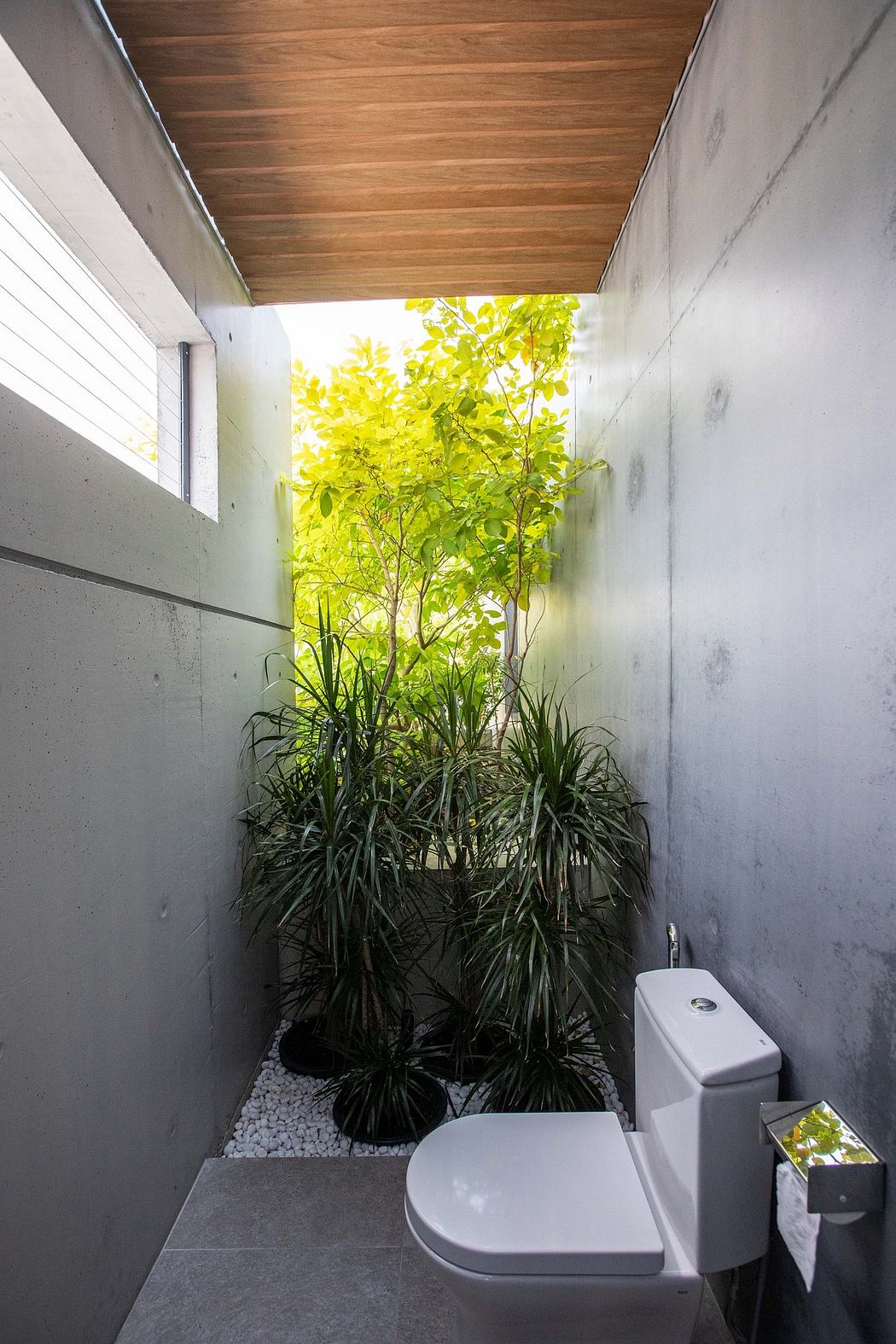 A cozy bathroom with a wooden ceiling, concrete walls, and lush greenery framing the view.