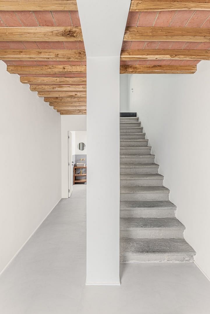 Minimalist staircase with exposed wood beams and concrete steps leading to a recessed doorway.