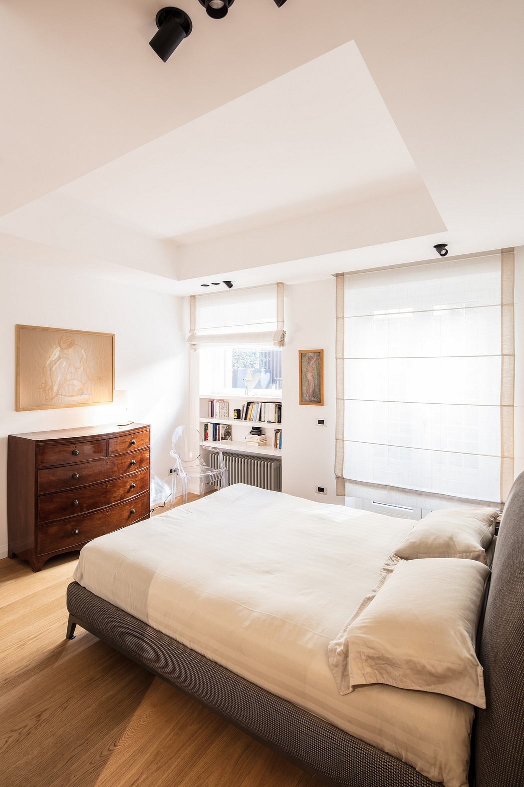 Cozy bedroom with wooden dresser, built-in bookshelf, and large window providing natural light.