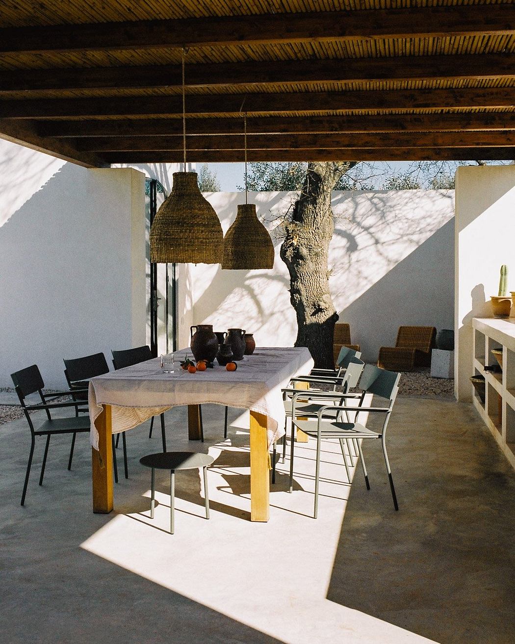 Rustic patio with wooden beams, hanging woven lamps, and a minimalist dining set on a tiled floor.