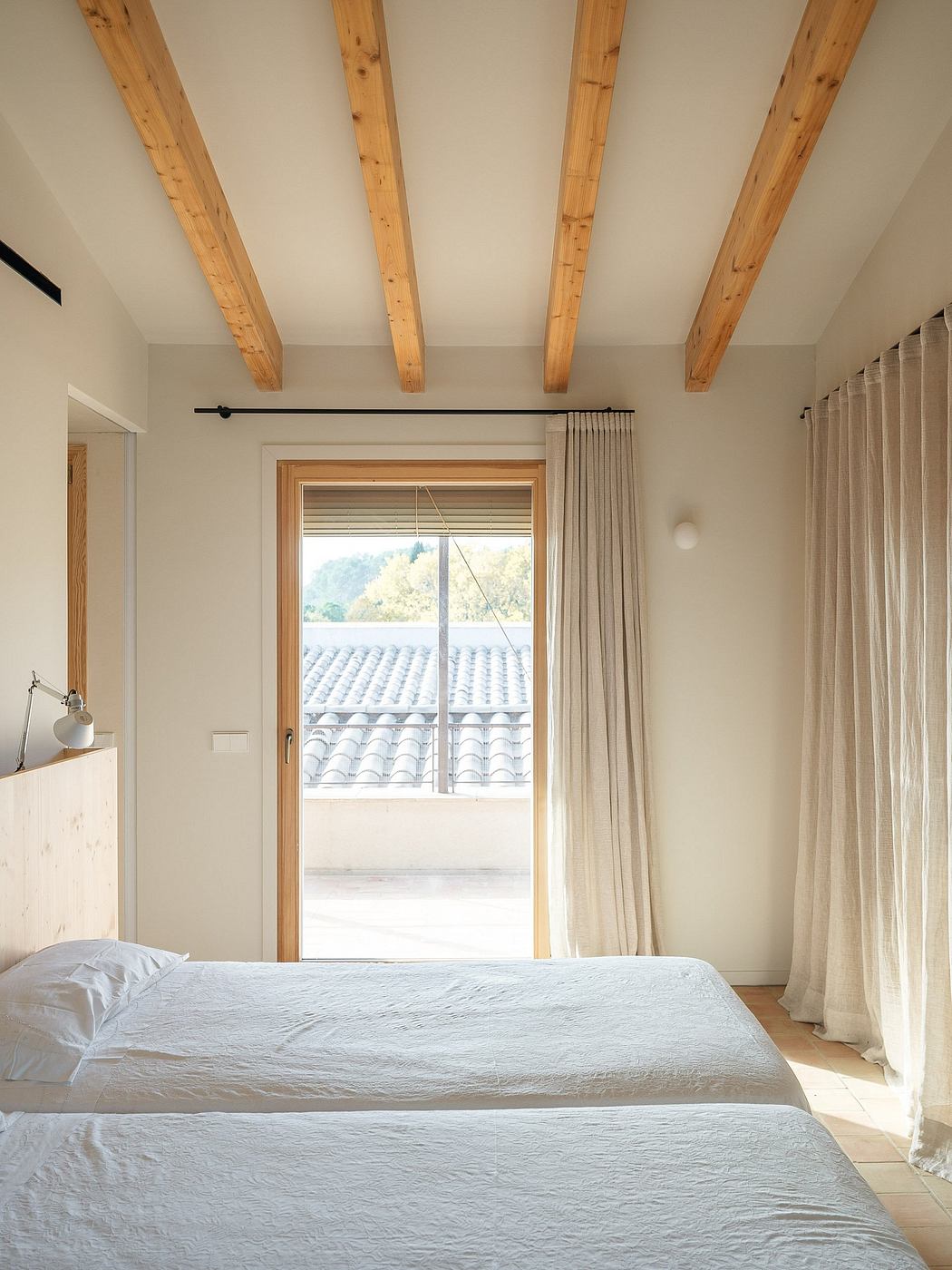 Minimalist bedroom with wood-beamed ceiling, large window, and neutral curtains.