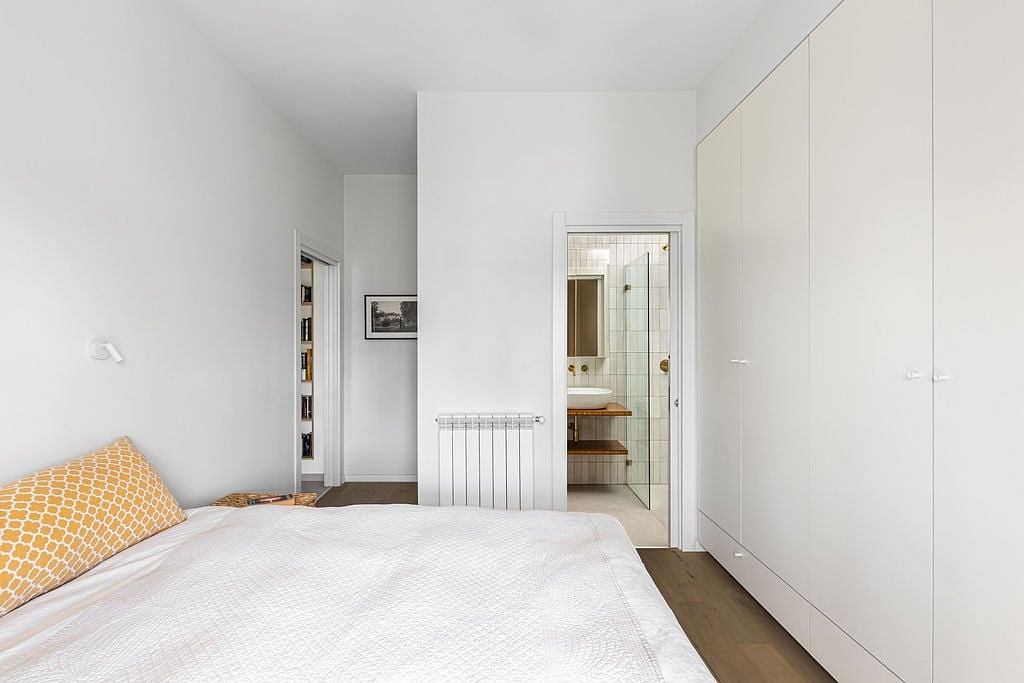 Bright, minimalist bedroom with white walls, built-in storage, and en-suite bathroom.
