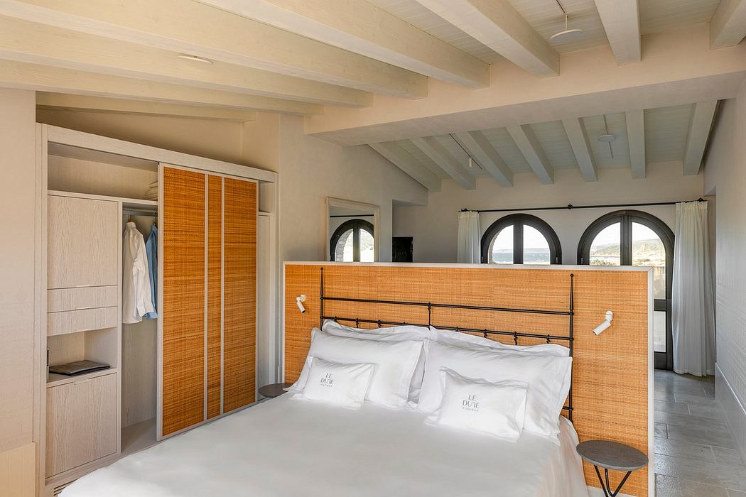 Spacious bedroom with wooden beams, arched windows, and modern, minimalist decor.