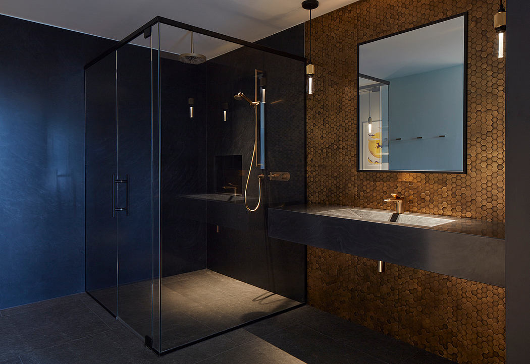 A modern, luxurious bathroom with dark tiled walls, glass shower enclosure, and gold-toned vanity.