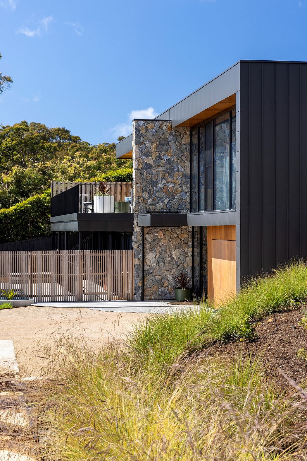 Modern, sleek architecture with stone facade, wooden accents, and lush landscaping.