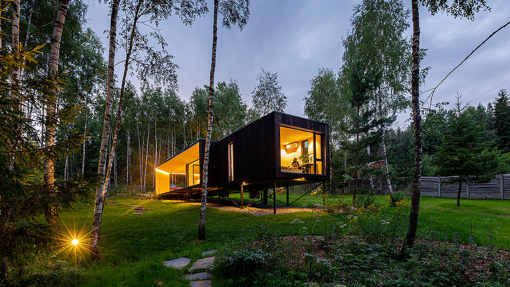 Modern black wooden cabin with large windows surrounded by trees and greenery.