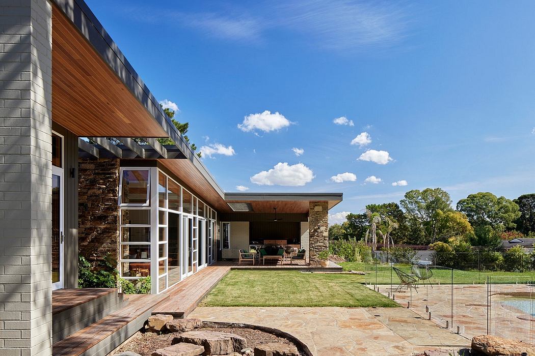 Modern, stone-and-wood exterior with large patio, lush greenery, and a pool visible.