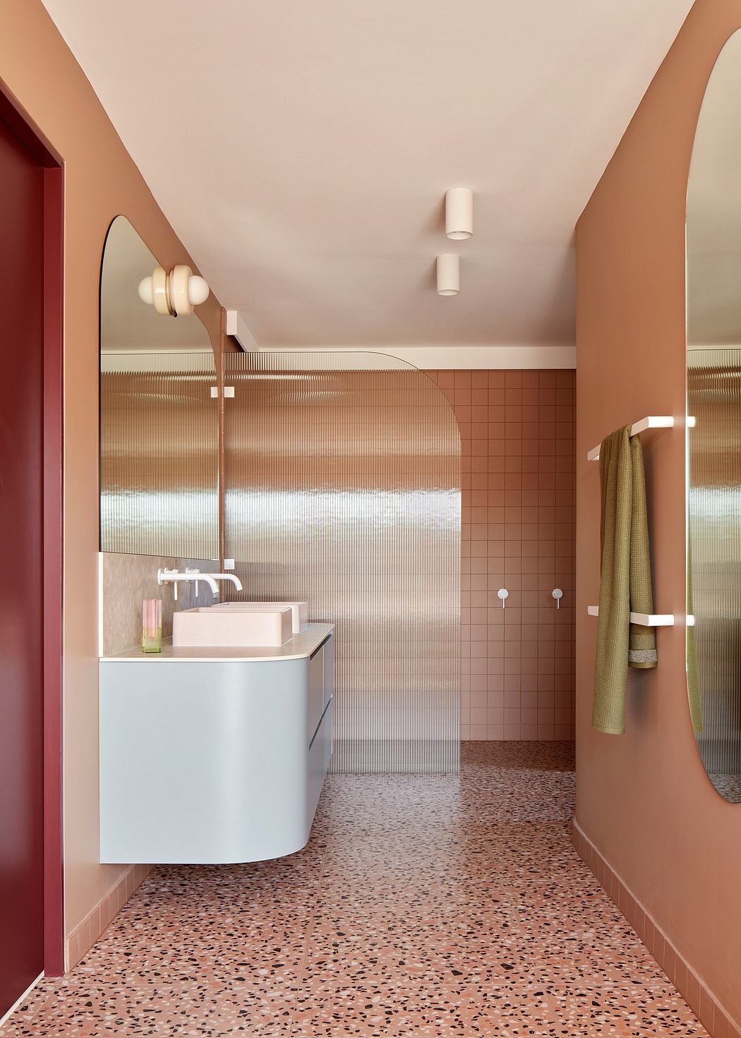 A minimalist bathroom with sleek curved mirrors, terracotta-colored tiles, and terrazzo flooring.
