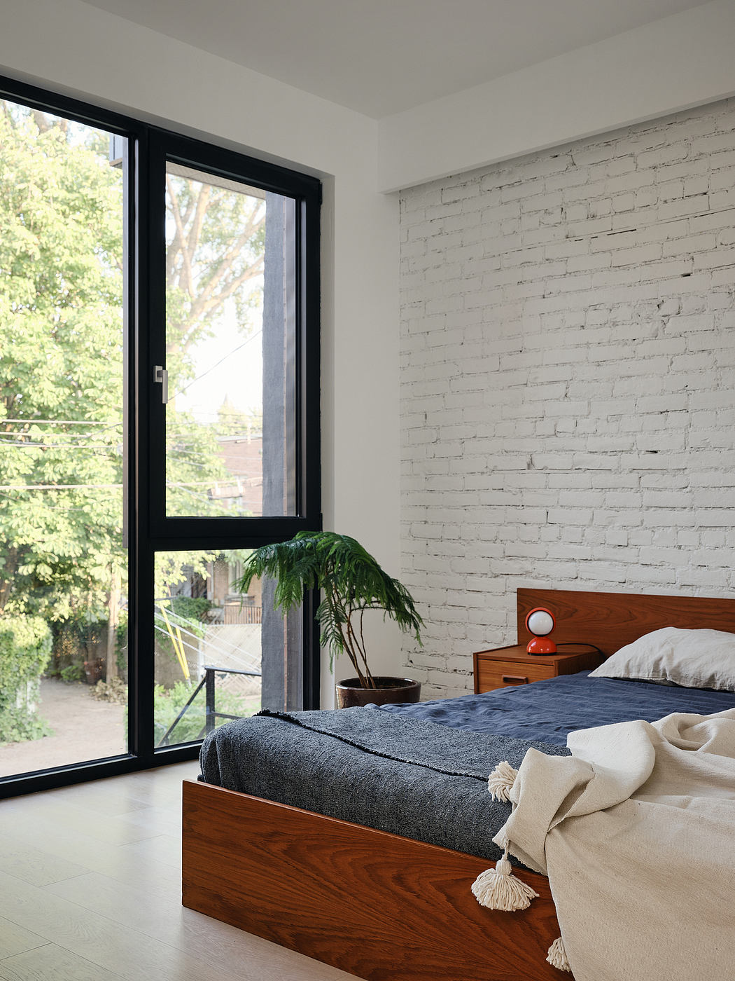Minimalist bedroom with white brick wall, large window, and wooden furniture.