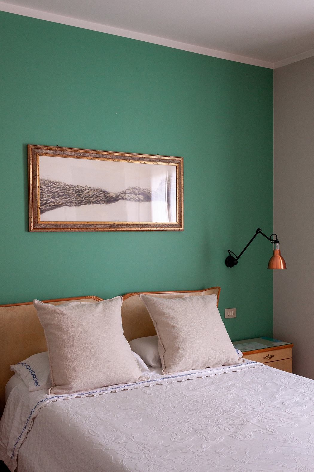 A cozy bedroom with a vibrant green wall, a framed artwork, and a plush bed with pillows.