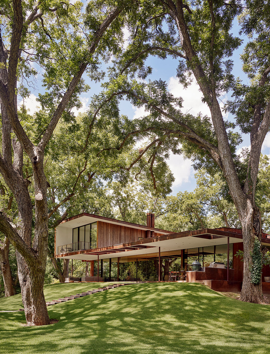 Modernist midcentury home nestled in lush, green landscape with overhanging trees.