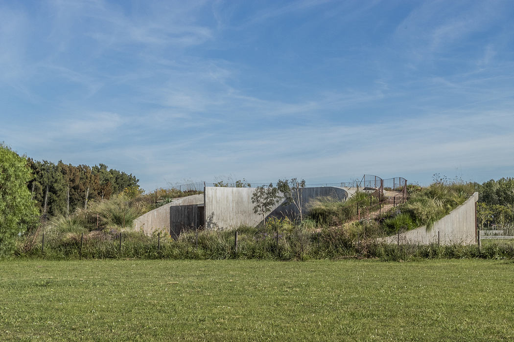 A modern concrete and steel structure nestled among green foliage, with a grassy foreground.