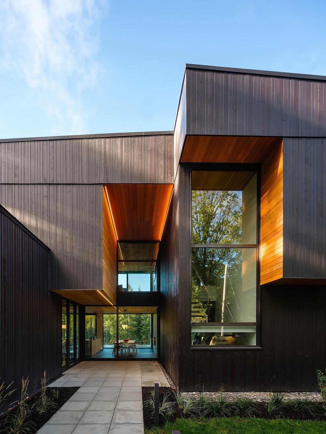 A modern, multi-level house with a mix of dark and warm wood paneling, large windows, and a patio.