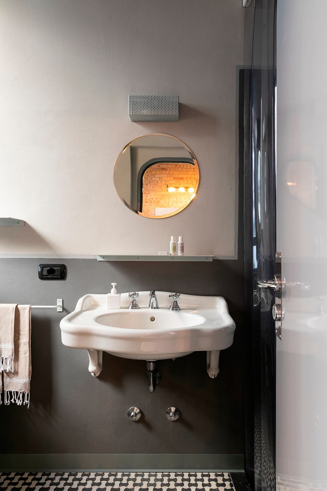 Sleek bathroom design with round mirror, minimalist fixtures, and patterned tile floor.