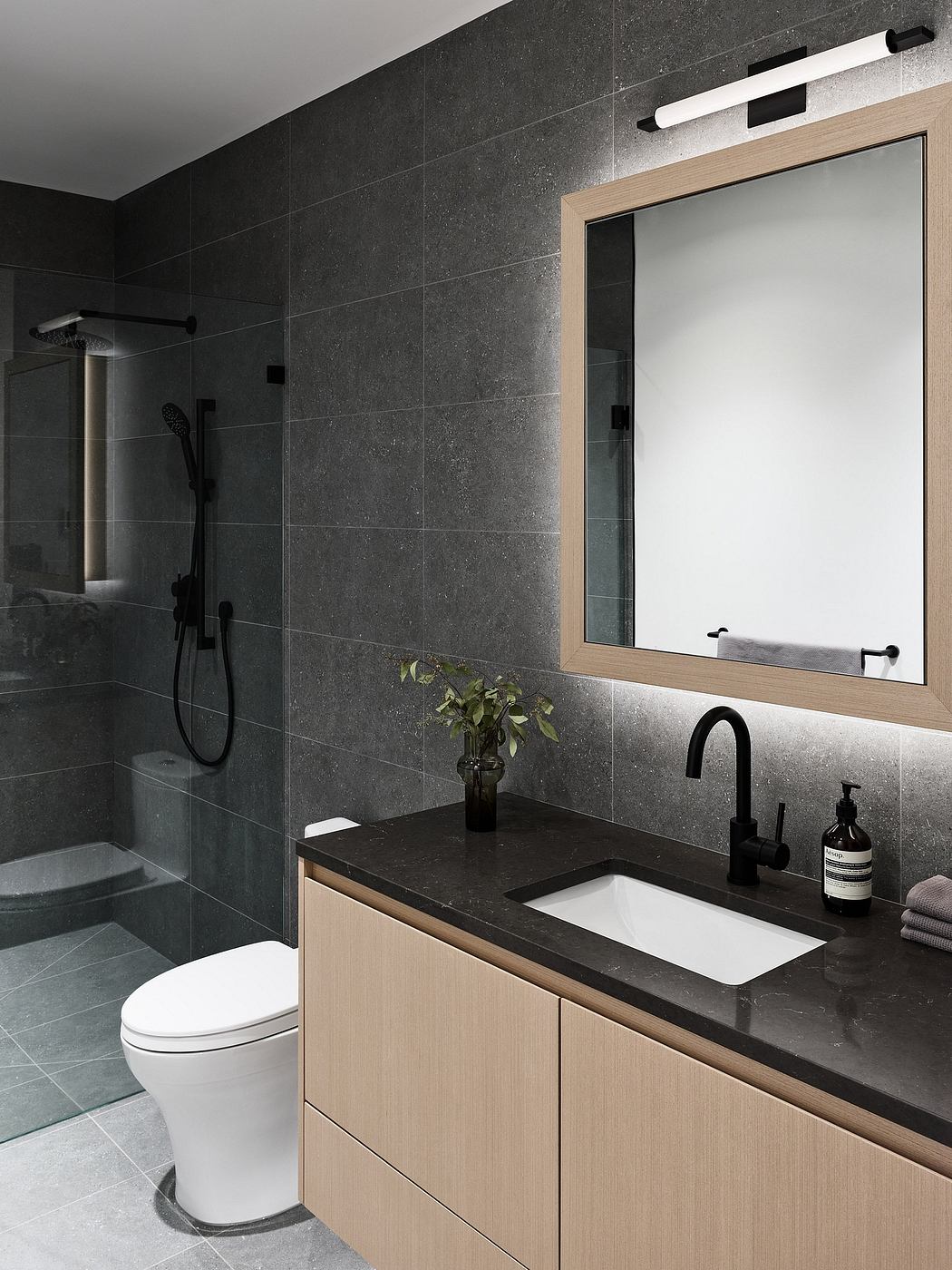 Sleek modern bathroom with dark tiled walls, wooden vanity, and black fixtures.