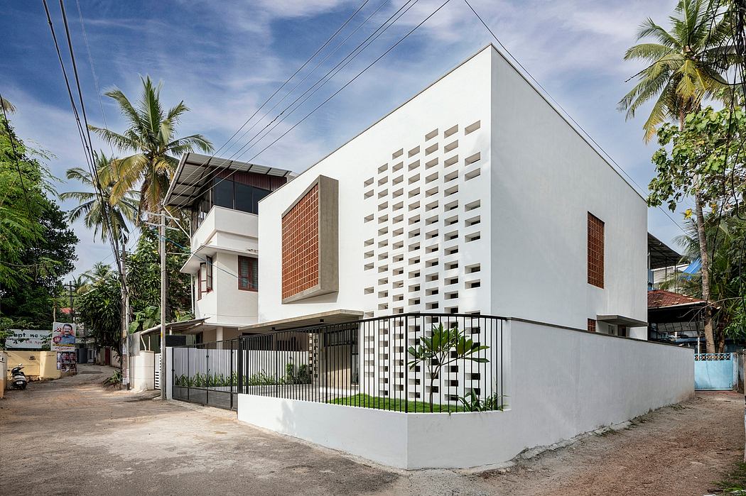 A modern, minimalist building with a mix of white walls and brick accents, surrounded by lush greenery.