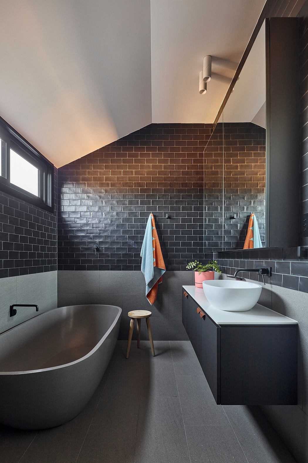 Sleek bathroom design with contrasting brick and gray tile walls, free-standing tub, and vanity.