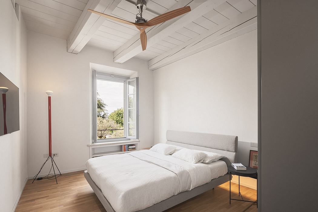 Bright, airy bedroom with wooden ceiling beams, large window, and minimalist furnishings.