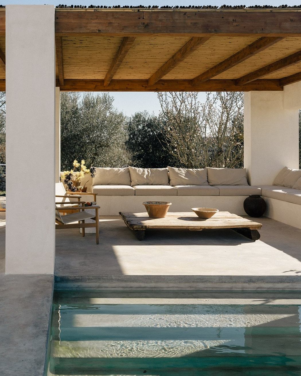 Rustic outdoor lounge area with wooden beams, plush sofas, and sleek concrete pool.