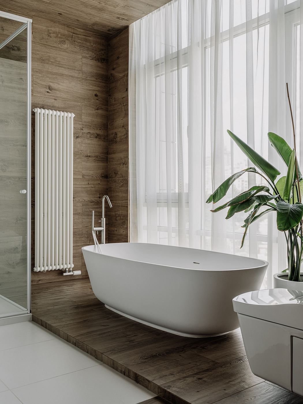 Rustic wood-paneled walls, freestanding bathtub, and lush plant decorate this modern bathroom.