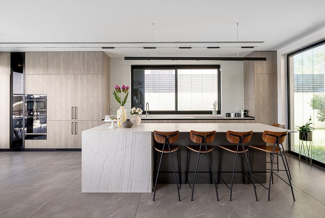 Modern, open-plan kitchen with marble countertop, wood cabinets, and sleek bar stools.