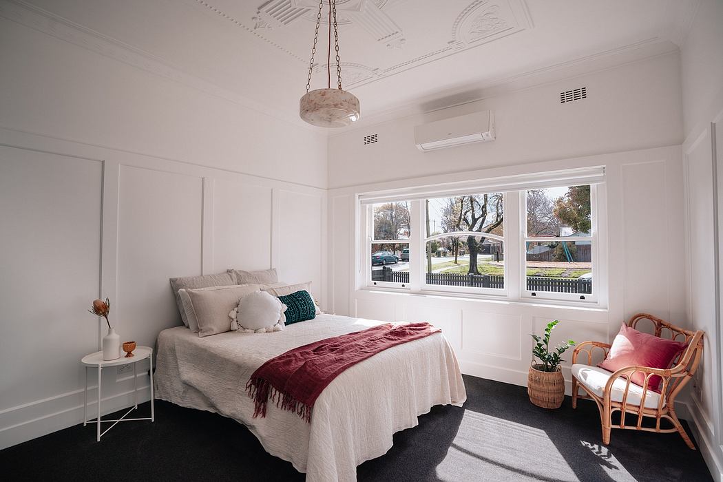 A cozy bedroom with large windows, white walls, and a unique hanging light fixture.