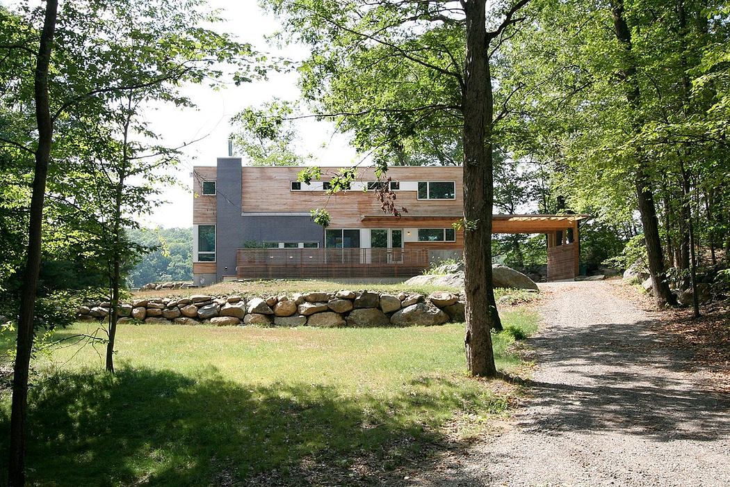 A modern, wooden-clad structure nestled in a lush, forested setting with a stone retaining wall.