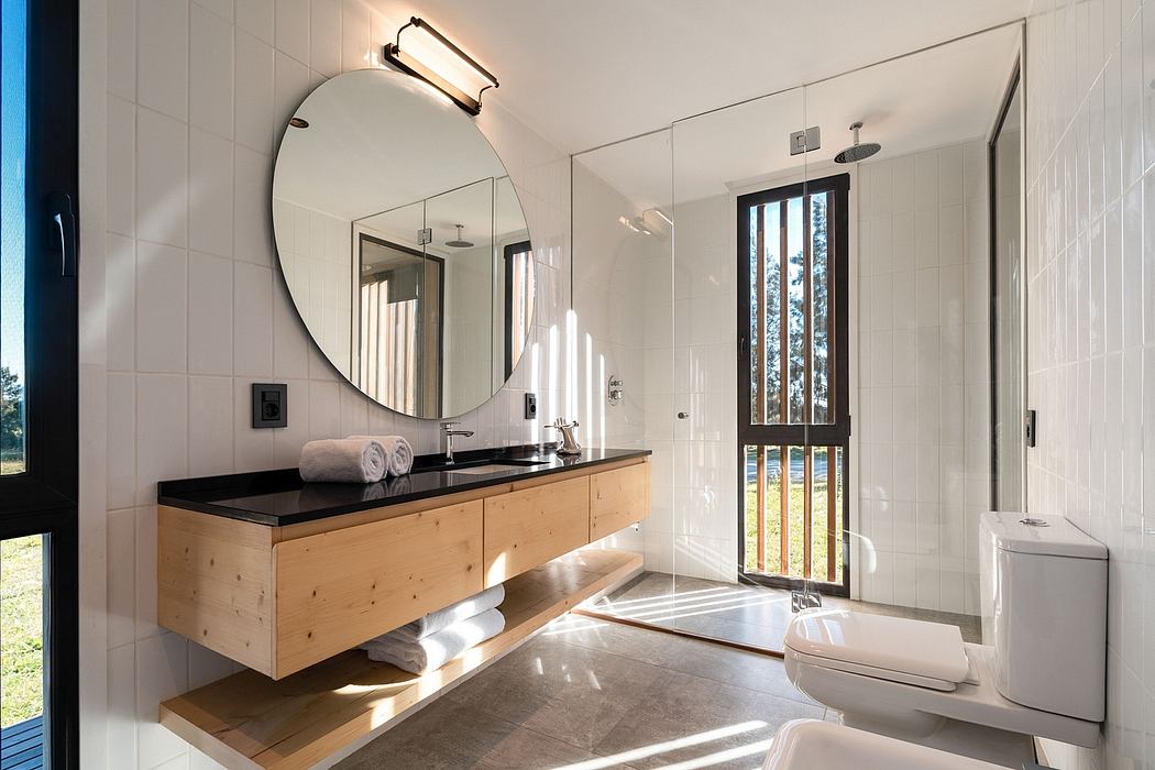 Modern bathroom with wood vanity, round mirror, and large window overlooking nature.