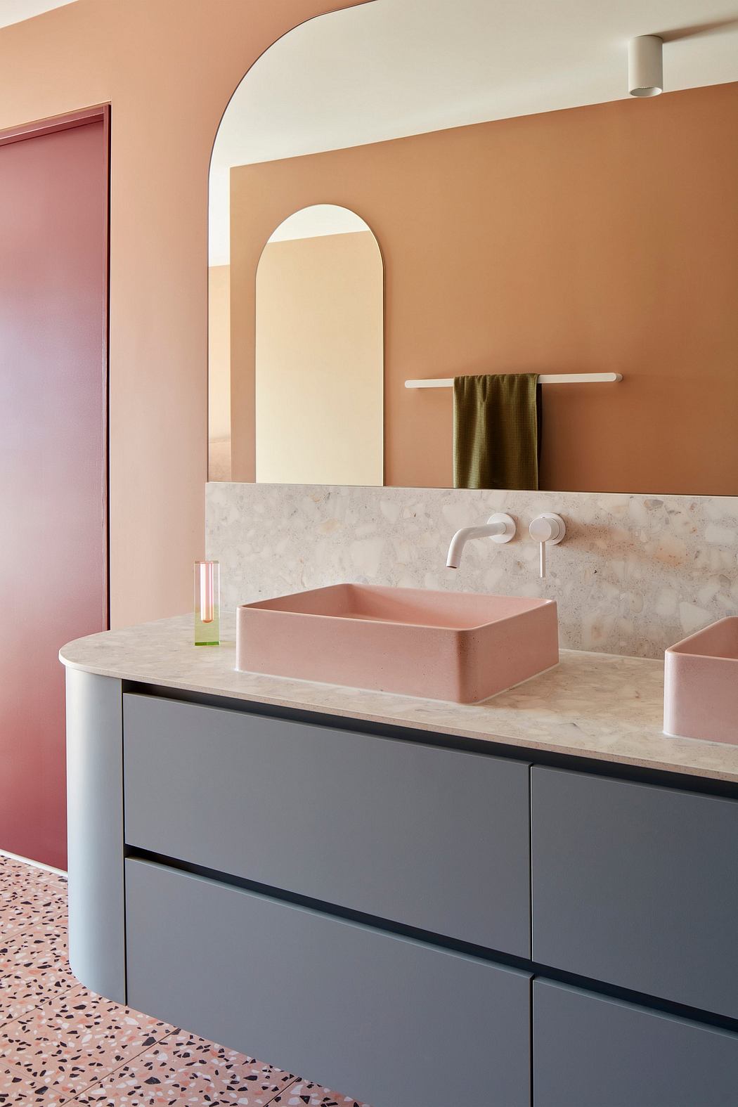 Stylish bathroom with marble countertop, pink vessel sink, and arched mirror.