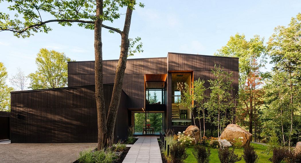 A modern, angular, wooden residence amid a lush, forested landscape.