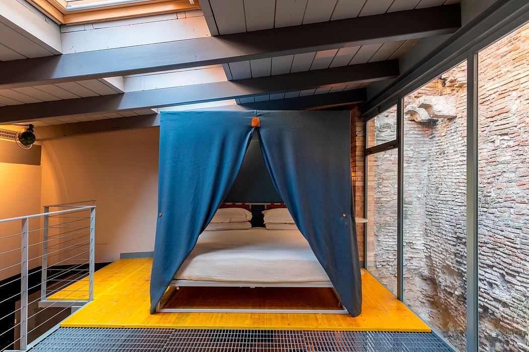 A modern, open-concept bedroom with a raised blue canopy bed and exposed wooden beams.