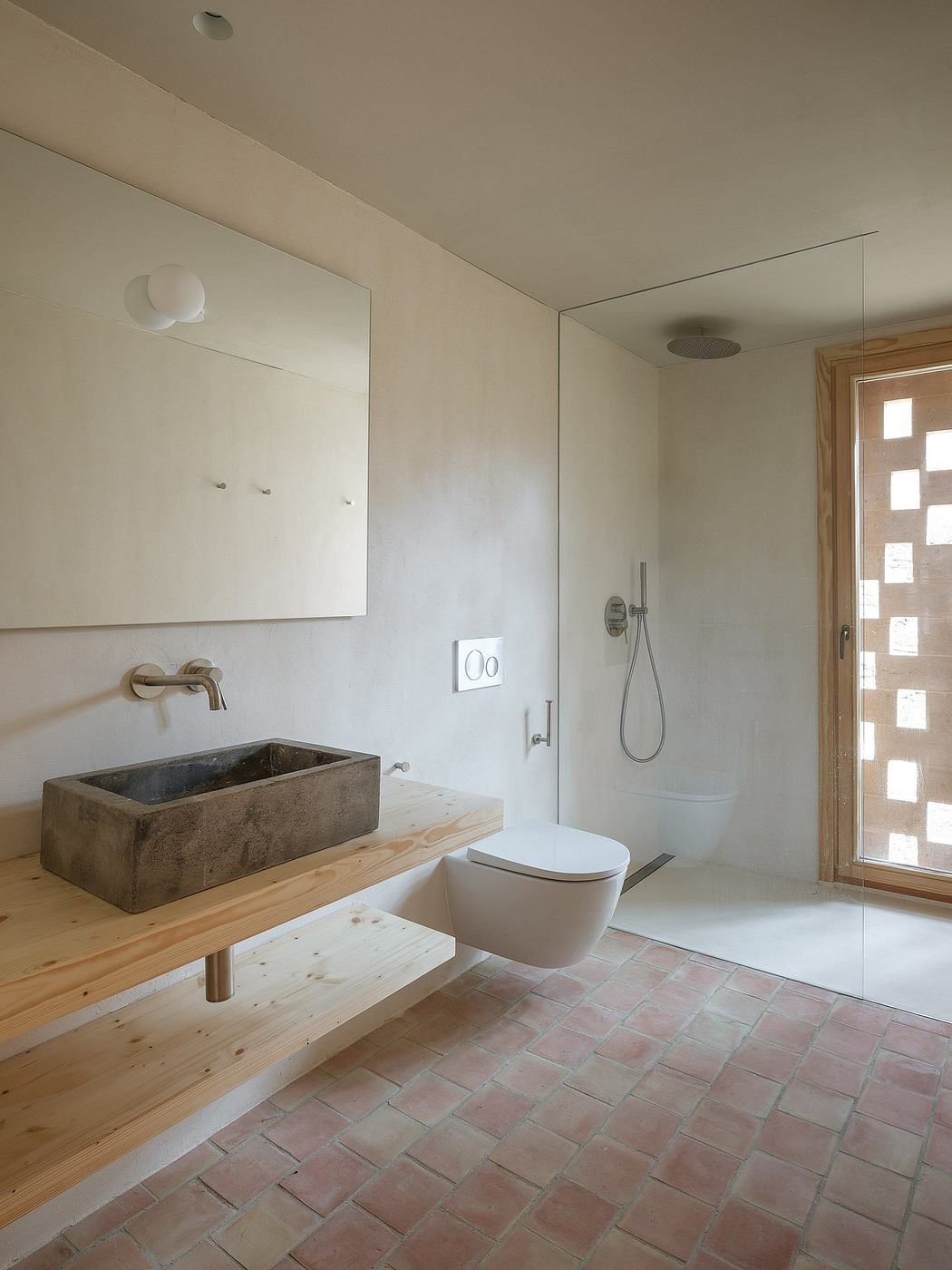 Minimalist bathroom with natural stone sink, wood vanity, and terracotta tile floor.