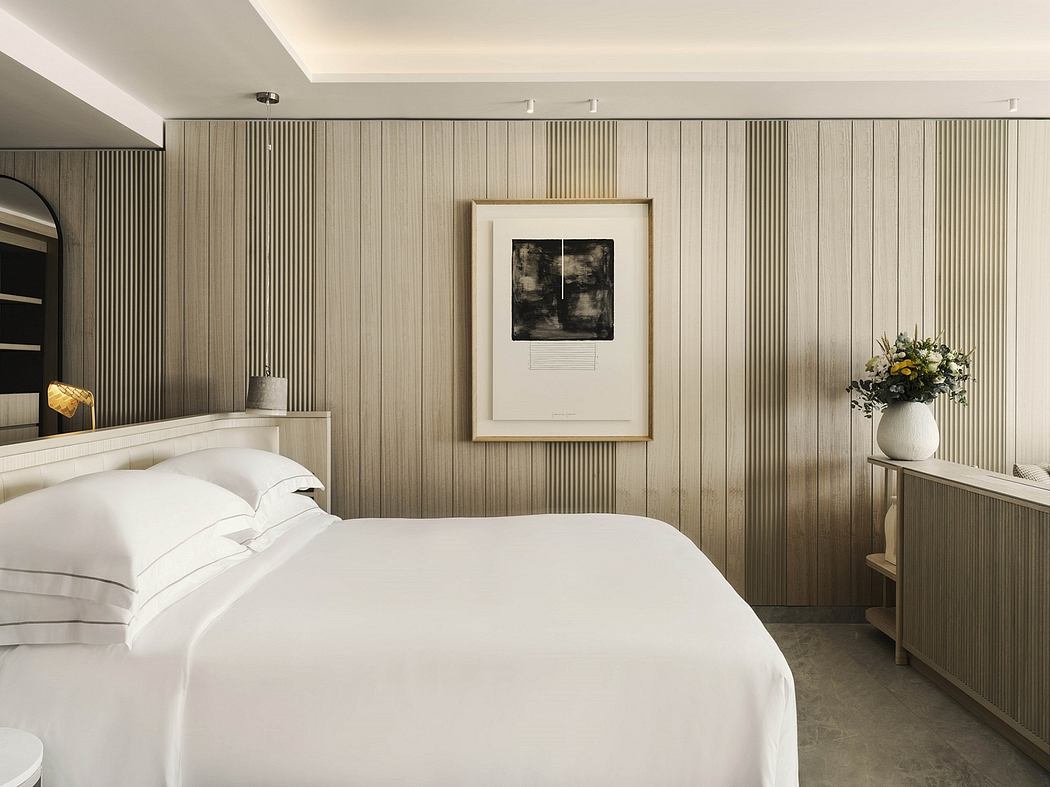 Minimalist bedroom with modern wood paneling, framed artwork, and a vase of flowers.