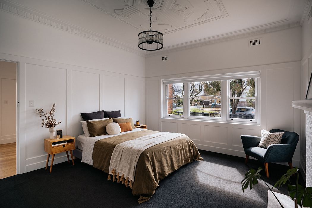 A spacious, ornate bedroom with large windows, elegant light fixture, and neutral decor.
