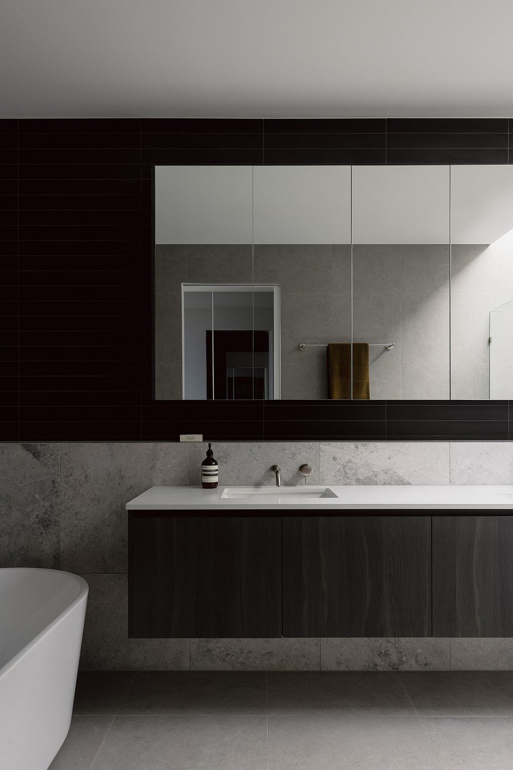 A stylish modern bathroom with dark cabinetry, white countertop, and minimalist fixtures.