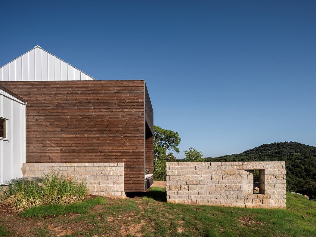Modern wooden facade with stone retaining walls, nestled in a lush, hilly landscape.
