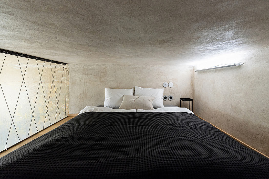 Minimalist bedroom interior with concrete walls, angular wood paneling, and a large black bedspread.