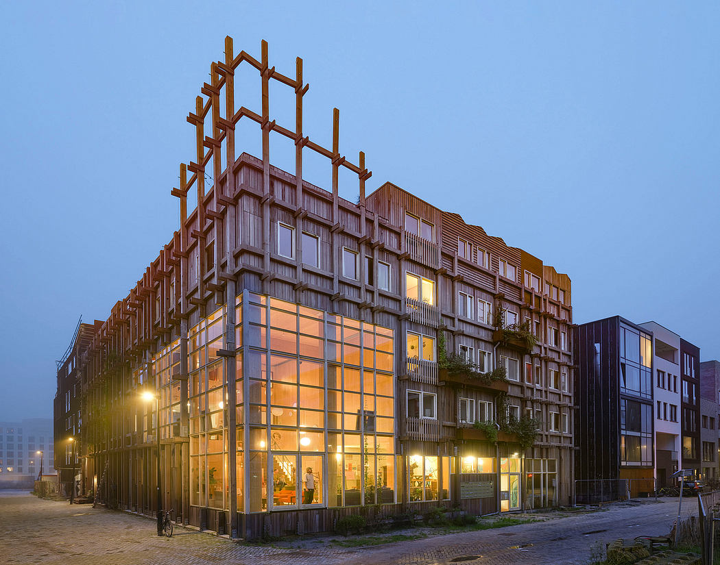A modern, multistory building with wooden beams and glass facades, illuminated at night.
