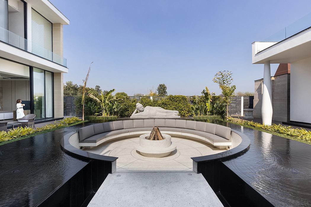 A modern outdoor patio with a circular seating area, water fountain, and lush greenery.
