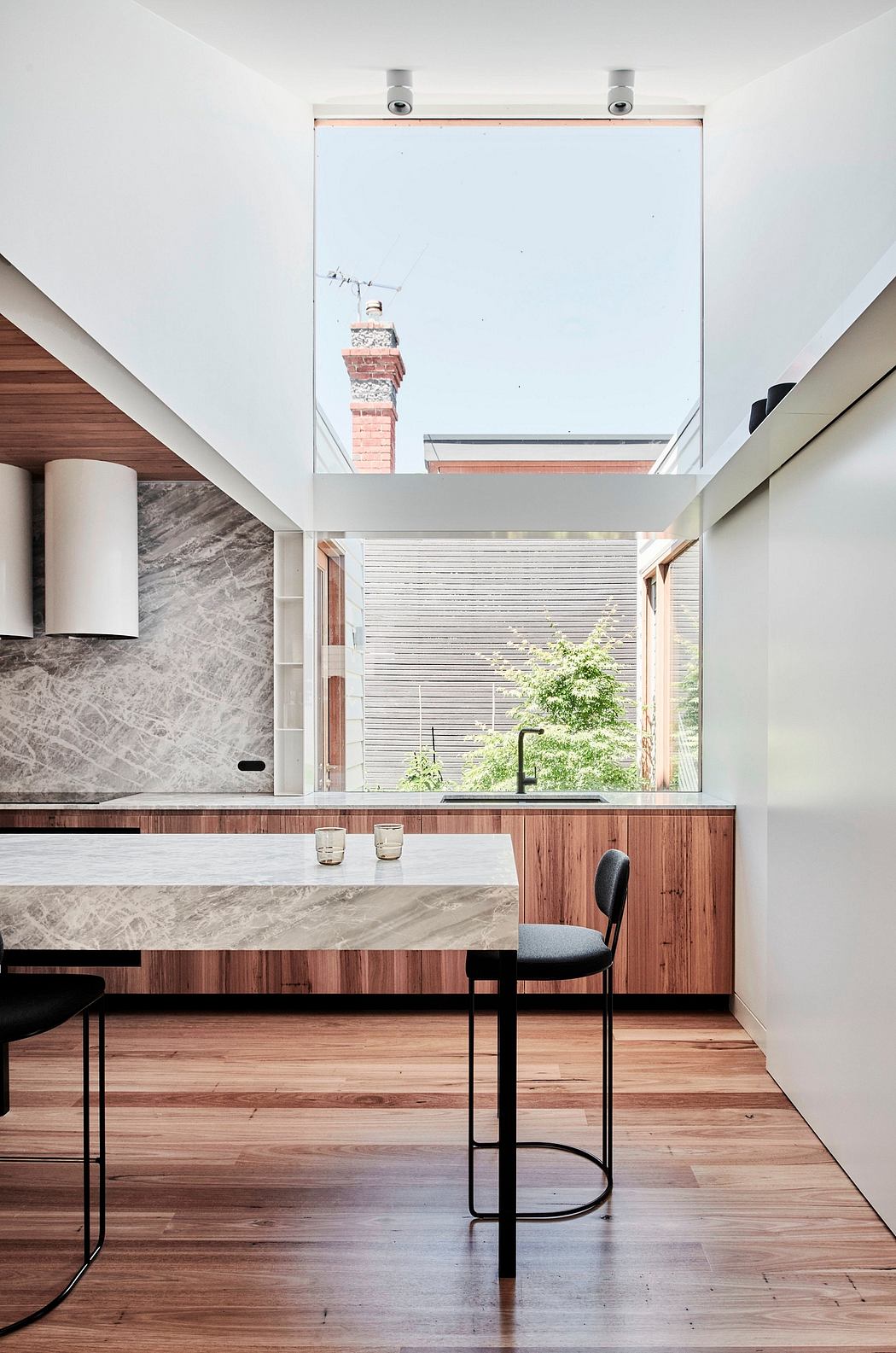Modern kitchen with wood and stone surfaces, skylights, and a view of the outdoor foliage.