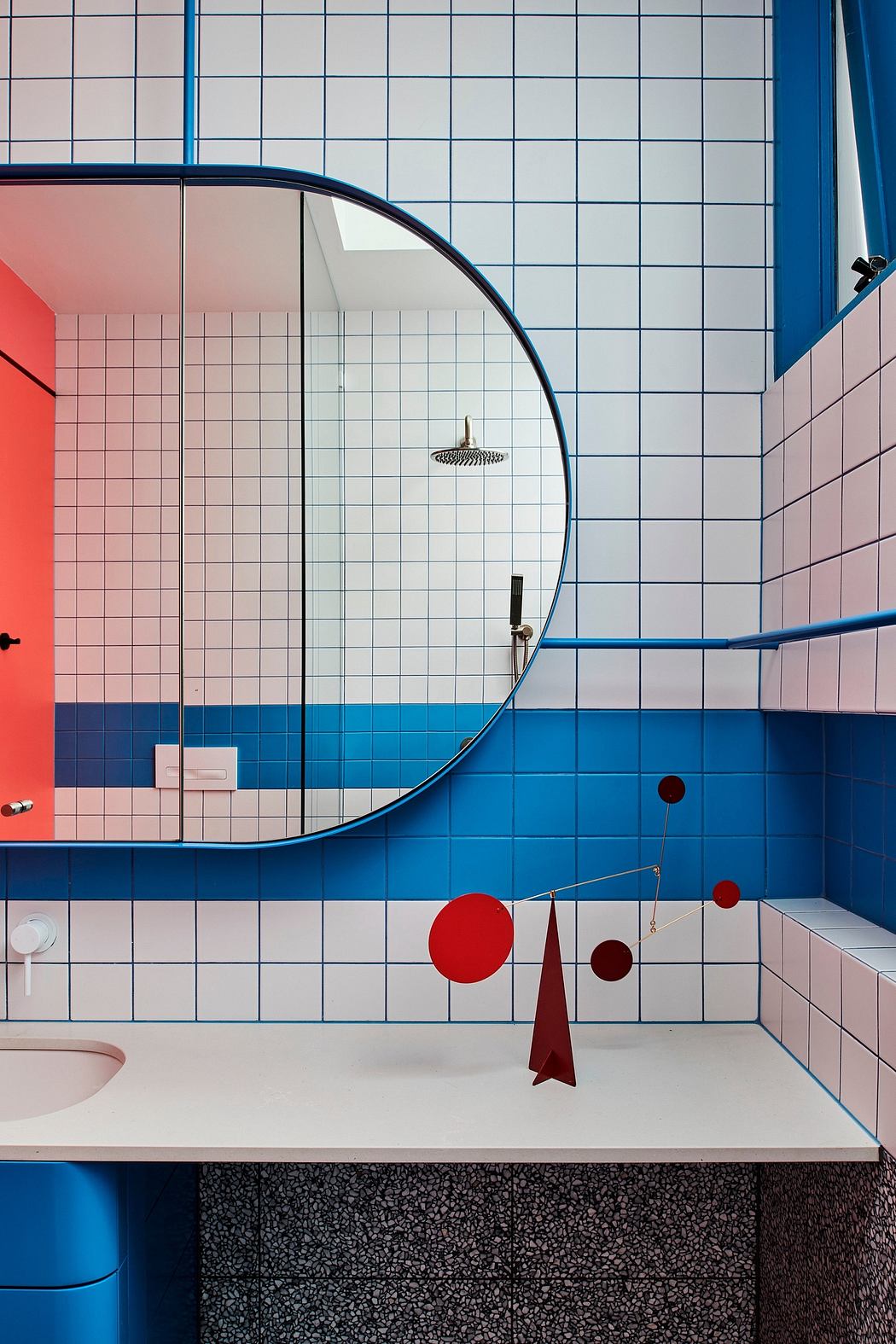Vibrant, geometric bathroom design with bold blue and pink tiles, circular mirrors, and sculptural red accents.