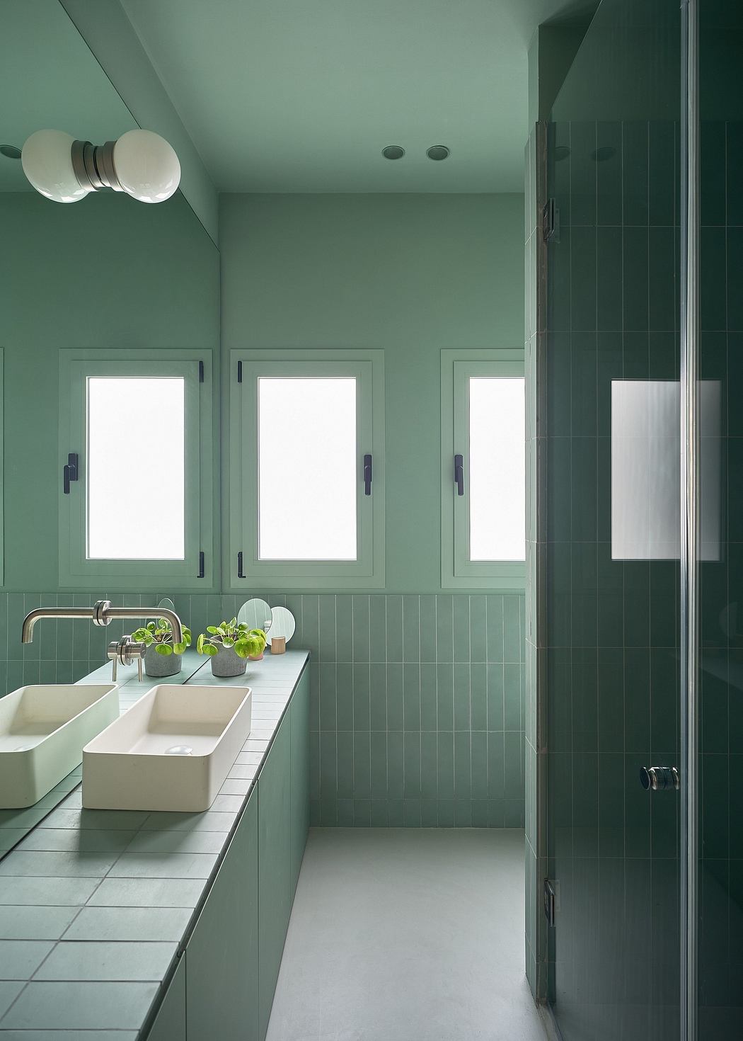 Minimalist bathroom design with monochromatic green tiles, dual sinks, and ample natural light.