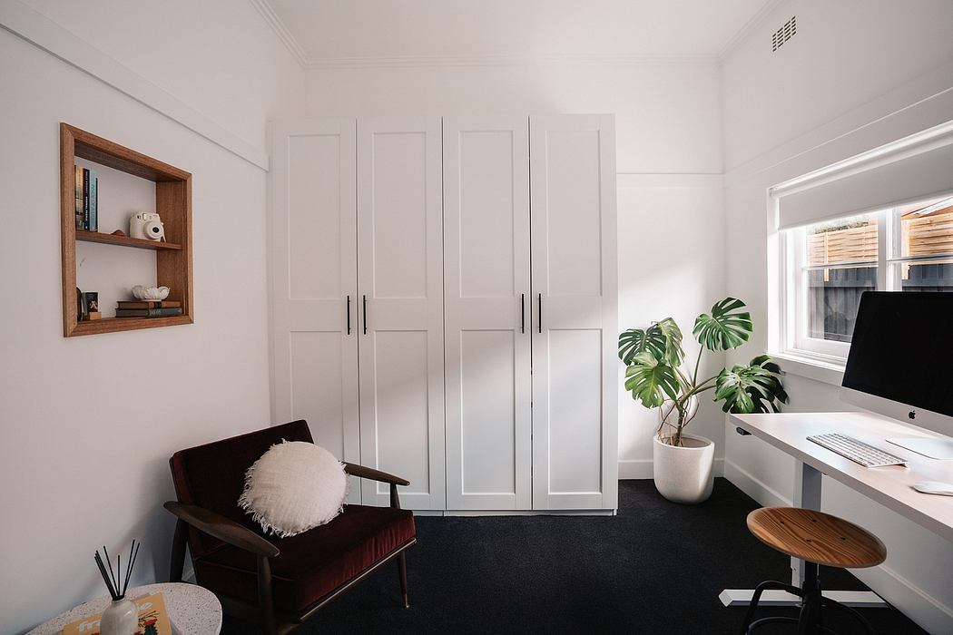 Minimalistic home office with built-in white closets, wooden shelves, and a potted plant.
