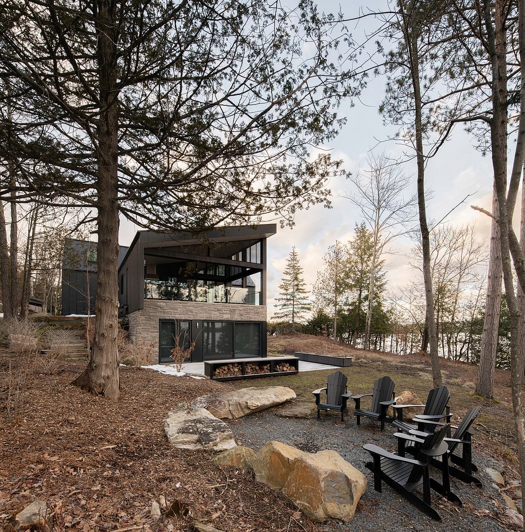 A modern, glass-walled cabin nestled in a wooded landscape, with a fireplace and cozy seating.