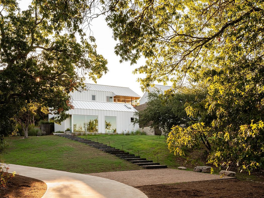 A modern, white-painted country home with a metal roof, surrounded by lush greenery.