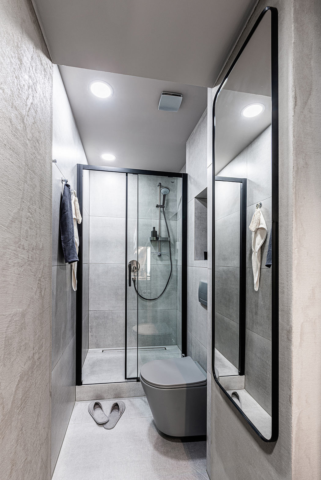 A modern, minimalist bathroom featuring a glass-enclosed shower, wall-mounted toilet, and recessed lighting.